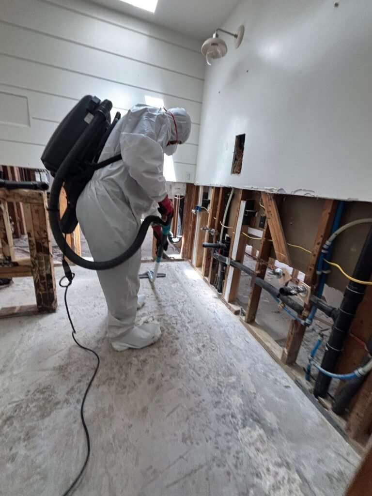 A technician with a backpack vacuum in a hallway with the walls opened and pipes visible in Santa Ana