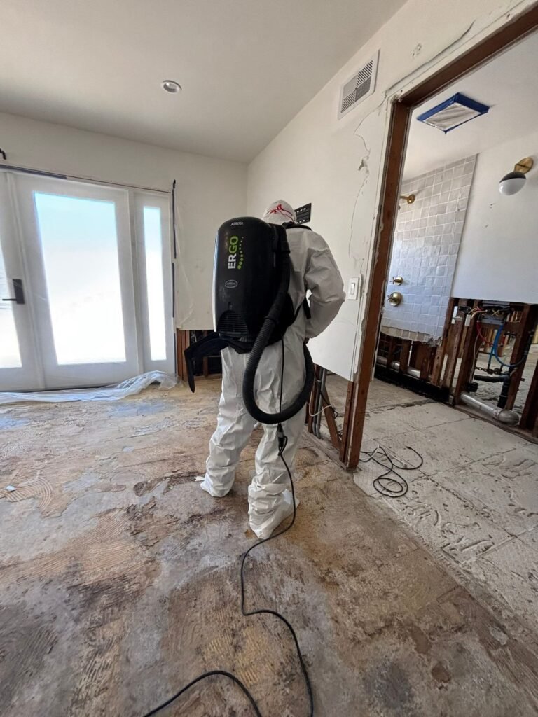 A technician with a backpack vacuum in a living room with the floor stripped and stained in Santa Ana