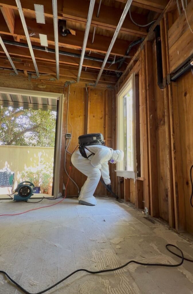 A technician with a backpack vacuum in a room opened to old board walls and joists in Santa Ana