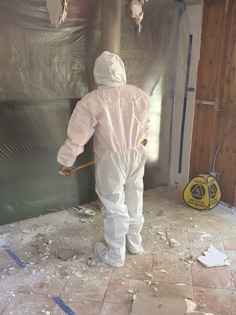 A suited technician inside plastic containment with debris across the tile in Santa Ana
