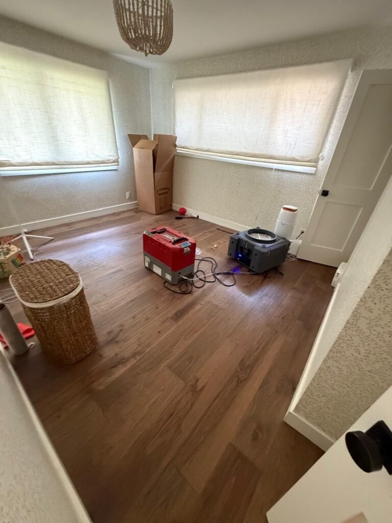 A furnished bedroom with a red dehumidifier and air mover on the hardwood in Santa Ana