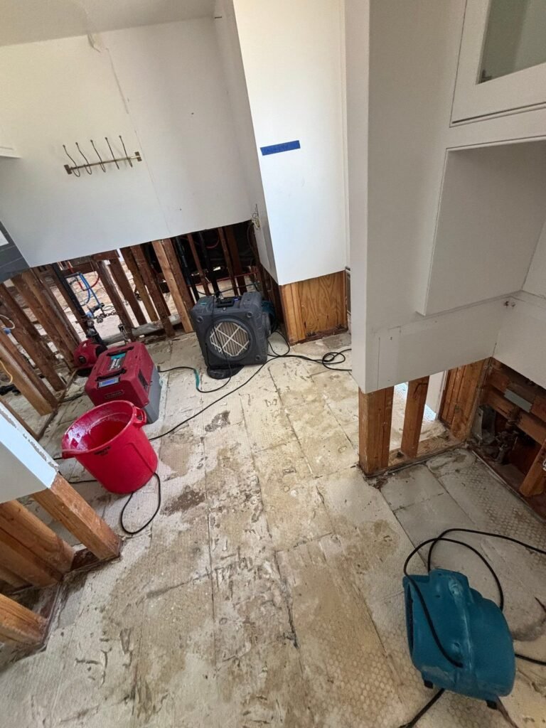A room with open walls, a red bucket, a black scrubber and a green air mover in Santa Ana