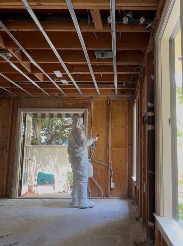 A technician spraying a doorway in a room opened to the joists in Santa Ana