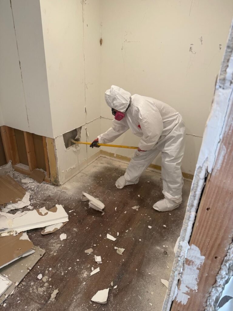 A technician pulling drywall with a pry bar, debris across the floor in Santa Ana