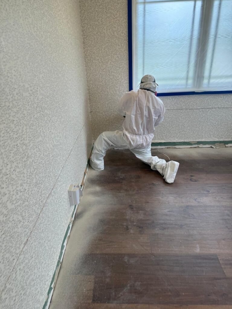 A technician kneeling to pull up laminate flooring along a taped wall in Santa Ana