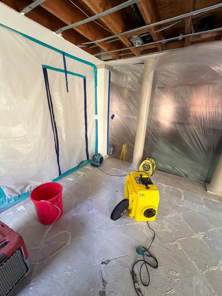 A room opened to the ceiling joists with containment, a yellow air mover and a red bucket in Santa Ana