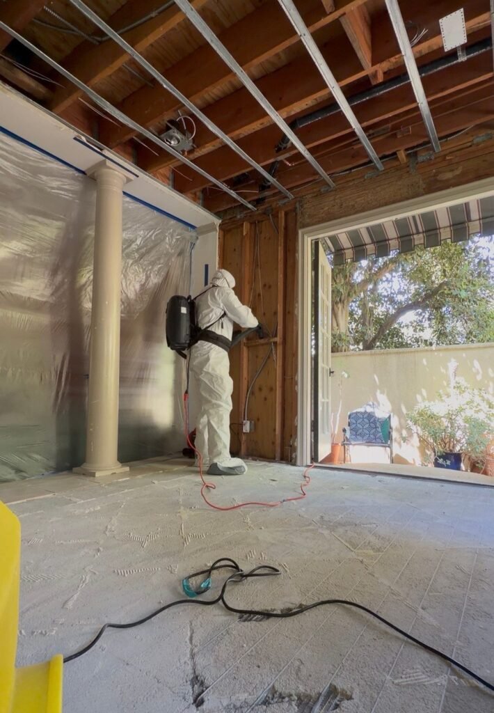 A technician spraying in a room with a picture window and the ceiling opened in Santa Ana